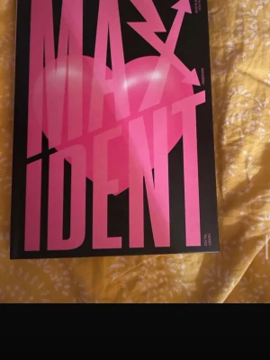 MAXIDENT av Stray Kids - MAXIDENT är en snygg bok med svart omslag och stora rosa bokstäver samt ett hjärta på framsidan. Boken är relaterad till K-popgruppen Stray Kids och har en modern, grafisk design. Perfekt för fans av gruppen eller dig som gillar coola samlarobjekt.