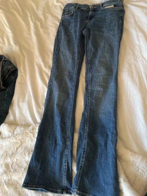 Blå bootcut jeans från Zara - Säljer ett par klassiska blå bootcut jeans från Zara. Jeansen har normal midja, dragkedja och knapp framtill samt fem fickor. Tillverkade i mjukt denimtyg som ger en skön passform och en tidlös look. Perfekta till sneakers eller boots. 