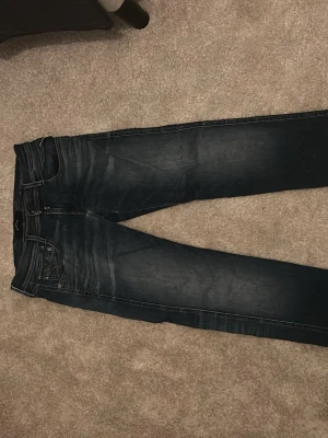 Mörkblå slim fit jeans - Snygga mörkblå slim fit jeans med slitningar och tvättade detaljer. Klassisk femficksmodell med dragkedja och knapp i midjan. 