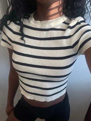 Randig croppad topp i bomull - Säljer en croppad topp med svarta och vita horisontella ränder. Toppen har korta ärmar, rund halsringning och är gjord i mjuk bomull. Perfekt till jeans eller shorts för en chill look.