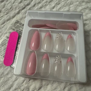 Press-on naglar rosa och fransk design - Snygga press-on naglar i mandelform med mix av helrosa och fransk manikyr med rosa tippar. Några naglar har vita blommor som dekoration. Kommer med en rosa nagelfil. Perfekt för dig som vill ha en trendig look.