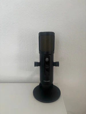 Svart gamingmikrofon DELTACO GAMING - Säljer en svart mikrofon från DELTACO GAMING med robust metallstativ och justerbara rattar på sidorna. Mikrofonen har flera reglage på framsidan och ett metallgaller upptill. Perfekt för streaming, gaming eller poddande.