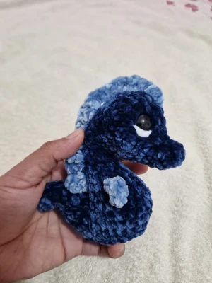 Blå virkad sjöhäst i plysch - Söt handgjord sjöhäst i mjuk plysch, virkad i mörkblått och ljusblått garn. Har stora svarta ögon med vit detalj och en man längs ryggen. Perfekt som dekoration eller gosedjur.