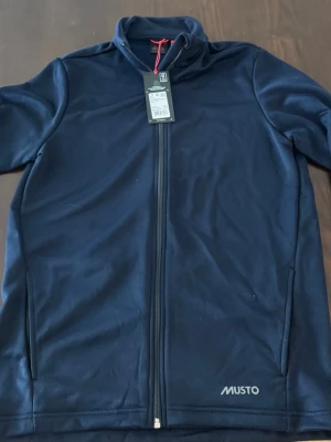 Musto tröja  - Musto sweatshirt med dragkedja. Ny med prislapp kvar, ej använd. Navy blå färg, storlek medium, herrtröja