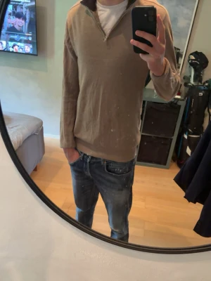 Beige halvzip tröja - Säljer en beige långärmad tröja med halv dragkedja i halsen. Tröjan har en avslappnad passform och ribbade muddar vid ärmslut och nederkant. Perfekt för lager på lager och enkel att matcha med jeans eller chinos.