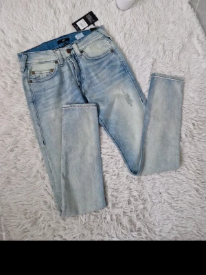 Ljusblå jeans från True religion  - Snygga ljusblå  jeans från True religion med slitningar på låret och klassisk femficksmodell. Jeansen har en något tvättad look och är tillverkade i bomullsblandning med stretch för extra komfort. Perfekta för en avslappnad och trendig stil.
