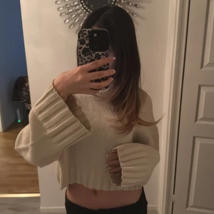 Beige croppad polotröja från Divided - Säljer en beige croppad polotröja från Divided med breda ribbade muddar vid ärmslut och nederkant. Tröjan har lång ärm och hög polokrage, perfekt för att hålla värmen under kyliga dagar. Stickad i mjukt material som känns skönt mot huden.