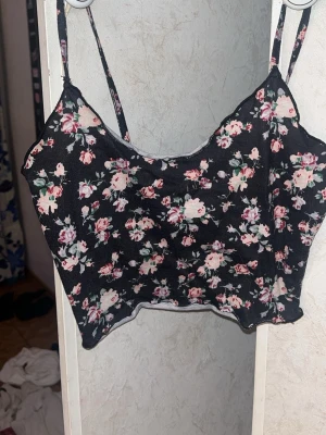 Blommig svart croptop från SHEIN - Snygg svart linnetopp/croptop från SHEIN med blommigt mönster i rosa, vitt och grönt. Toppen har tunna axelband och croppad passform. St Xs men är en kort topp! 