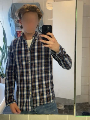 Blårutig skjorta från Bondelid - Säljer en klassisk blårutig skjorta från Bondelid med vita och röda detaljer. Skjortan har lång ärm, knappar framtill och en avslappnad passform. Tillverkad i mjuk bomull som är skön att bära till jeans eller chinos.