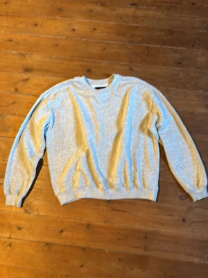 Ljusgrå sweatshirt med rund hals - En basic ljusgrå sweatshirt med rund halsringning och långa ärmar. Tröjan har ribbade muddar vid ärmslut och nederkant för en klassisk look. Perfekt att matcha med jeans eller joggers för en avslappnad stil.