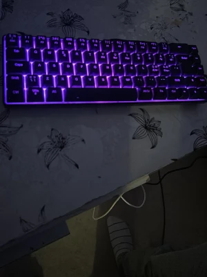 RGB-bakgrundsbelyst tangentbord - Säljer ett kompakt tangentbord med RGB-belysning som kan växla mellan olika färger, bland annat lila och blått. Tangentbordet har en smidig design och ansluts via kabel. Perfekt för gaming eller studier och ger snygg effekt i mörkret.