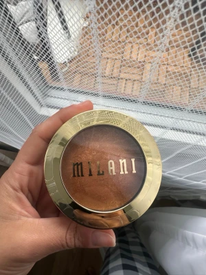Milani Baked Bronzer 05 Soleil - Milani Baked Bronzer i nyansen 05 Soleil ger en varm, gyllene glow med skimrande finish. Kommer i en rund guld- och plastförpackning med transparent lock. Perfekt för att skapa solkysst look och highlighta ansiktet. Plasten är på 