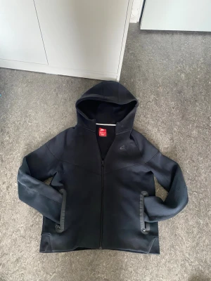 Svart nike tech junior storlek (158-170cm) - Säljer en svart hoodie från Nike med hel dragkedja framtill och diskret Nike-logga på bröstet. Hoodien har huva och två fickor med dragkedja. Tillverkad i mjukt och bekvämt material. Står XL men känns som S när du har på dig dom eftersom det är junior storlek och inte reguljär storlek 