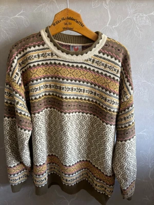 Mönstrad stickad tröja  - Stickad tröja med klassiskt mönster i beige, brunt, gult och rosa . Rund halsringning och ribbade muddar. Tröjan har ett retroinspirerat flerfärgstryck och är perfekt för dig som gillar vintagevibbar och sköna material.