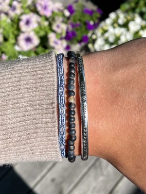 Armbands set - Säljer ett snyggt set med tre armband: ett blåvitt flätat band, ett pärlarmband med mörka och ljusa pärlor samt ett silverfärgat metallarmband med ingraverade detaljer. Perfekt för dig som gillar att mixa olika stilar och material. Alla armband är justerbara och sitter inte ihop men säljs som ett set. Perfekt till sommaren☀️