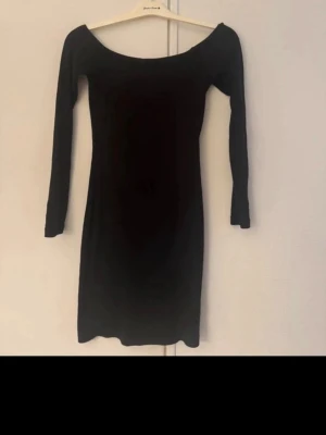 Svart offshoulder klänning Bik Bok - En svart, tight offshoulder klänning från Bik Bok i storlek XS. Klänningen har långärmade ärmar och en kroppsnära passform som framhäver siluetten. Perfekt för dig som gillar stilrena och enkla plagg.
