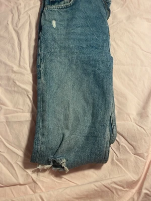 Blå slitna jeans med hål - Säljer ett par ljusblå jeans med slitningar och hål på knäna och låret. Jeansen har en rak/baggy passform och högmidja, har dock lite skav längst ner på byxbenet. Knappt använda och vet tyvärr inte storlek då lappen är borta men skulle gissa på xs-s. 