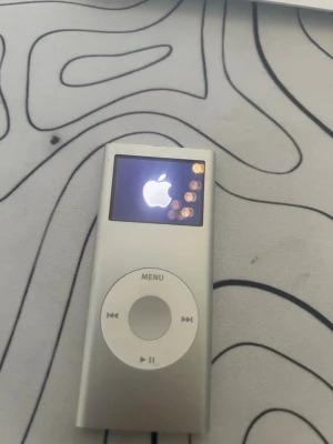 Apple iPod Nano silver - Klassisk Apple iPod Nano i silver med vit klickhjul och liten färgskärm. Perfekt för att lyssna på musik på språng. Smidig och lätt design i metall och plast, enkel att använda med tydliga knappar och display. FUNKAR BRA.