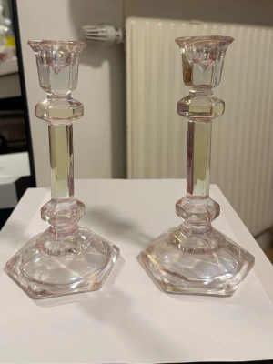 Sexkantiga ljusstakar i glas - Två stilrena ljusstakar i transparent glas med svag rosa ton. De har sexkantig fot och kantiga detaljer längs stommen som ger en klassisk men modern känsla. Perfekta som dekoration på bordet eller i fönstret.