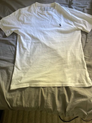 Vit t-shirt från Polo Ralph Lauren - Klassisk vit t-shirt från Polo Ralph Lauren med den ikoniska lilla loggan broderad på bröstet. T-shirten har rund hals, korta ärmar och är gjord i mjuk bomull för en skön känsla. Perfekt basplagg till garderoben.