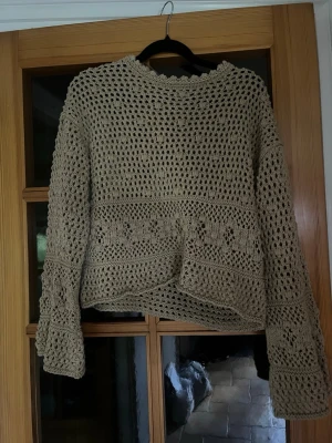 Beige virkad tröja med mönster från Zara - Säljer en beige, handvirkad tröja med lång ärm och hålmönster. Tröjan har ett unikt virkat blommönster runt midjan och ärmarna, samt vågig kant vid halsen. Perfekt för lager på lager och en avslappnad stil.