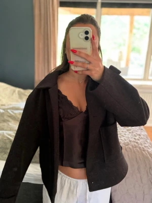 Svart ulljacka med knappar - Stilren svart  jacka i ull med klassisk krage och stora knappar framtill. Jackan har en croppad passform och raka ärmar, perfekt för dig som gillar en enkel men trendig look.