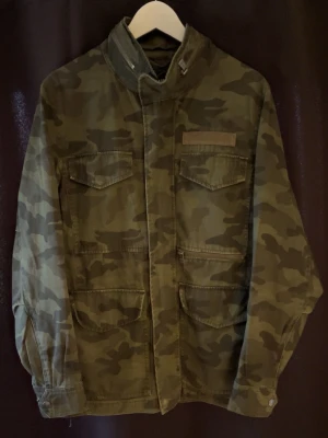 Fieldjacka camouflage - Tjo säljer en snygg camouflage Fieldjacka i gröna toner med flera fickor framtill och hög krage. Jackan har ett klassiskt militärinspirerat mönster och stängs med dragkedja och tryckknappar. Perfekt för dig som gillar Grisch och lite av den nya nya stilen! Märker är only and sons och storlek S! Passar 175-182cm lång! Skicket är mycket bra och inga defekter🤩hör av dig vid minsta fråga eller fundering! Mvh Premium fashion😁