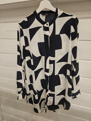 Mönstrad skjorta - Snygg skjorta med grafiskt svartvitt mönster och knappar framtill. Skjortan har lång ärm och klassisk kortare krage, perfekt för dig som gillar en modern och stilren look. Materialet känns lätt och luftigt. Längre modell går under rumpan på mig som är 164cm. Liten minimalistisk fläck baktill, se bild har inte provat att tvätta.