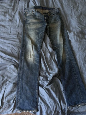 Blå raka jeans från Levi's - Säljer ett par klassiska blå jeans från Levi's med raka ben och slitna detaljer. Jeansen har en snygg tvätt med ljusare partier framtill och bakfickor med den ikoniska Levi's-lappen. Perfekta för en avslappnad och trendig look.