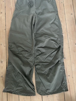 Militärgröna vida parachutebyxor från Zara - Från Zara med bred passform och snöre i midjan. Byxorna har en avslappnad look och är tillverkade i ett tunt, mjukt material som känns skönt mot huden. 