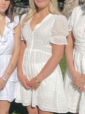 Vit broderad kortklänning med puffärm - Superfin vit kortklänning med broderade detaljer och v-ringning. Klänningen har puffärmar och knappar framtill, samt en lätt utsvängd kjol. Perfekt för sommarens alla tillfällen och ger en romantisk känsla. Endast använd en gång! 