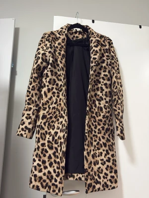 Leopardmönstrad fuskpälsjacka - Säljer en lång, leopardmönstrad fuskpälsjacka med svart innerfoder. Jackan har rak passform, diskret krage och stängs framtill. Perfekt statement-plagg för dig som vill sticka ut i vinter och hålla dig varm.