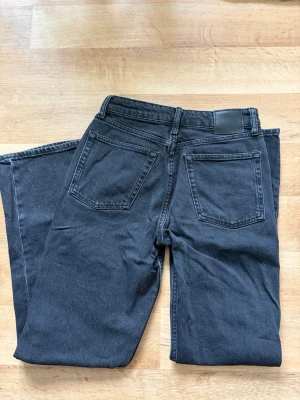 Svarta raka jeans från Cubus  - Säljer ett par svarta raka jeans från Cubus med klassisk femficksmodell och hög midja. Jeansen har en stilren look med svarta sömmar och en patch bak i midjan. Perfekta till en avslappnad streetwear-stil.