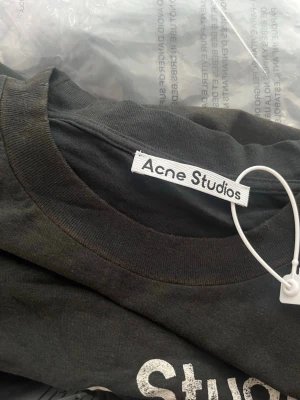 Svart Acne Studios t-shirt - Snygg svart t-shirt från Acne Studios med tryck på bröstet där det står 'Acne Studios STOCKHOLM 1996' i vitt. Klassisk rund halsringning och korta ärmar. Perfekt basplagg med clean design och street vibe.