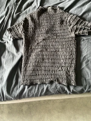 Grå ribbad t-shirt med struktur - Unik svart t-shirt med korta ärmar och coolt ribbat strukturmönster över hela plagget. Materialet känns stretchigt och ger en modern vibe. Perfekt för dig som vill sticka ut lite extra med din stil.
