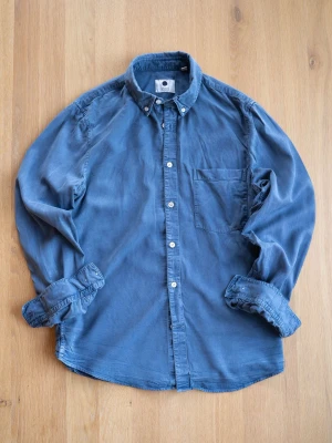 Blå skjorta från NN07 i bomull - Snygg blå skjorta från NN07 i mjuk bomull. Klassisk button-down krage, bröstficka och vita knappar framtill. Perfekt till jeans eller chinos för en clean och avslappnad stil.