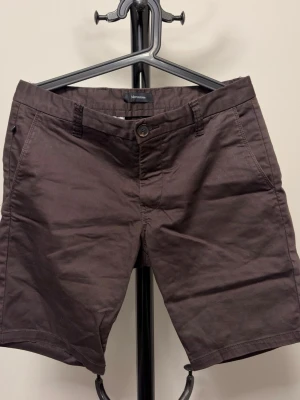 Bruna shorts från Matinique - Snygga bruna shorts från Matinique med klassisk passform och knappgylf. Tillverkade i ett mjukt bomullsmaterial som känns skönt mot huden. Perfekta för varma dagar och har praktiska sidofickor samt hällor för bälte.