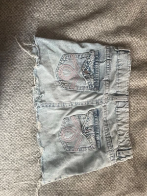 Ljus jeanskjol från Gina Tricot - Säljer en ljusblå jeanskjol från Gina Tricot med rå kant och slitna detaljer. Kjolen har två bakfickor med dekorativa sömmar i rosa och klassisk jeanslook. Perfekt för dig som gillar en avslappnad och trendig stil.