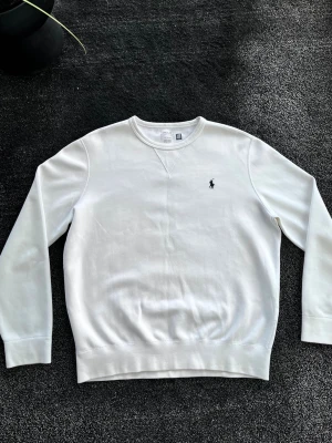 Ralph Lauren sweatshirt  - Klassisk vit sweatshirt från Polo Ralph Lauren med rund halsringning och diskret broderad logga på bröstet. Tröjan har långa ärmar och ribbade muddar vid ärmslut och nederkant. Perfekt för en clean och stilren look. Skick 10/10, Storlek L, KÖP GÄRNA BUNDLE (20%rabatt på allt!!!) ✅