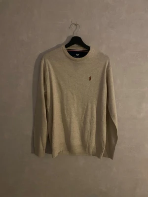 Beige stickad tröja från Ralph Lauren - Beige stickad tröja från Ralph Lauren med rund halsringning och klassisk broderad logga på bröstet. Långärmad modell i mjukt material, perfekt för lager-på-lager och enkel att matcha med jeans eller chinos. Står 3XL av någon anledning men sitter som L.