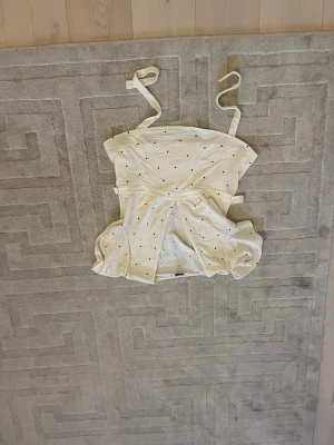 Vit prickig linnetopp från Gina Tricot - Supersöt vit linnetopp från Gina Tricot med små svarta prickar. Toppen har tunna axelband som knyts och en lätt puffig form nedtill. Perfekt för en fräsch och trendig sommarlook!