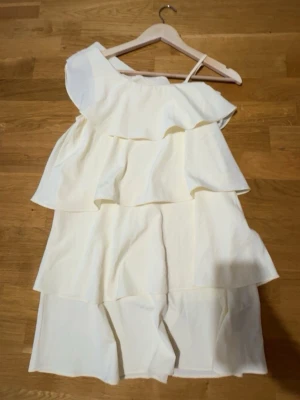 Vit omlottklänning med volanger - Säljer en vit kortklänning med flera lager volanger och oneshoulder-design. Anvdänds 2 gånger och superfint skick, pris går även att diskuteras.