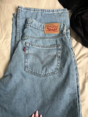 Levi's Superlow ljusblå jeans - Säljer ett par klassiska ljusblå Levi's Superlow jeans med raka ben och femficksmodell. Jeansen har den ikoniska röda Levi's-lappen på bakfickan och patch i läder bak i midjan. Tillverkade i slitstark denim, perfekta för en avslappnad look.pris kan diskuteras😊