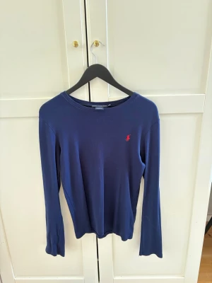 Marinblå långärmad tröja Ralph Lauren - Klassisk marinblå långärmad tröja från Ralph Lauren Sport i 100% bomull. Tröjan har rund halsringning och den ikoniska röda logotypen broderad på bröstet. Perfekt för en stilren och avslappnad look. Storlek L, men jag som tjej i storlek S kan använda. Såklart är den lång och lite stor men det ser inte hemskt ut. Passar både killar och tjejer, luftigt material. 