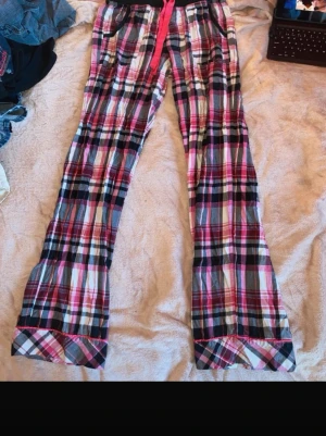 Rutiga pyjamasbyxor med rosa band - Säljer ett par mysiga pyjamasbyxor i rutigt mönster med färgerna rosa, svart, vitt och grått. Byxorna har resår i midjan, ett rosa knytband och fickor framtill. Passar storlek XS/S, skriv gärna vid frågor!💕