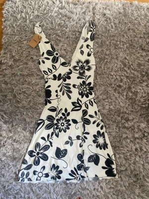 Vit blommig kortklänning från Sellpy - Snygg vit kortklänning med svart blommigt mönster från Sellpy. Klänningen har v-ringning och är ärmlös, perfekt för varma dagar. Materialet känns lätt och skönt mot huden. Passar dig som vill ha en fräsch och trendig look.