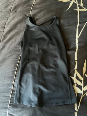 Tränings linne - Säljer en svart linnetopp med smala axelband och snygg knytning i ryggen. Toppen har en enkel och stilren design med en liten vit logga baktill. Skulle säga att den är i storlek S. Aldrig använt.