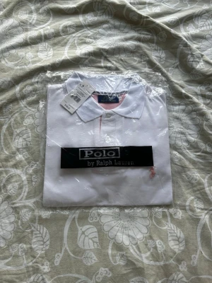 Vit Ralph Lauren Pike  - Säljer en stilren vit piké från Polo Ralph Lauren i storlek S. Klassisk modell med rosa broderad logga och rosa detaljer på insidan av kragen. Helt ny med prislapp kvar. Mvh William🙌