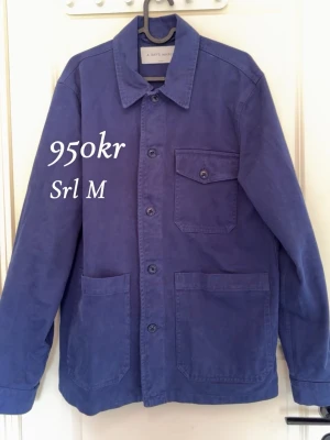 Blå overshirt från A Day's March - Säljer en stilren blå overshirt från A Day's March. Skjortjackan har klassisk krage, knäppning framtill, en bröstficka med lock och två stora fickor nedtill. Perfekt lager-på-lager-plagg i bomull med avslappnad passform.