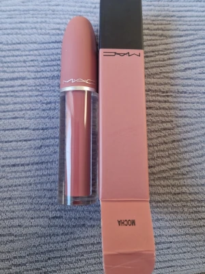 MAC Mocha nude läppstift - MAC Mocha läppstift i en snygg nude-brun nyans. Hylsan har en matt finish i matchande färg och genomskinlig nederdel som visar färgen. Kommer i originalförpackning. Perfekt för dig som gillar naturliga toner och stilren design.